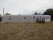 2008 Ford Focus - A long, gray mobile home sits on a foundation with dry grass in the foreground under an overcast sky.