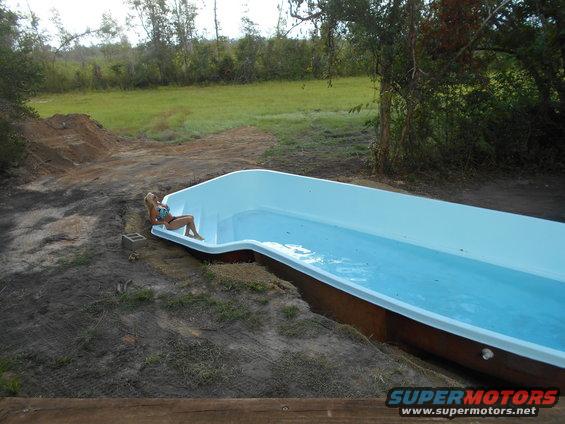 Woman in bikini sits on the edge of an empty swimming pool installation
