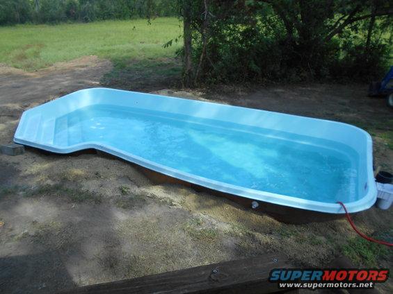 above-ground pool filled with blue water, set in a grassy yard with trees in background. Supermotors.net logo visible