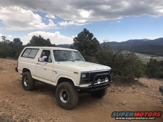 White Ford Bronco parked on a dirt road with hills in the background