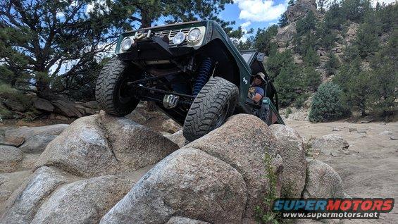 Green 1966 Ford Bronco climbing large rocks on a trail