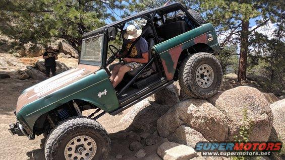 Green Ford Bronco off-roading over rocks, front fender has '4x4' badge