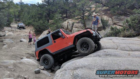 Orange Jeep Wrangler TJ navigating rocky terrain, 3q-front view