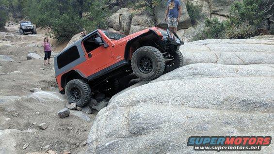 Orange Jeep Wrangler navigating a rocky trail with another vehicle in the background