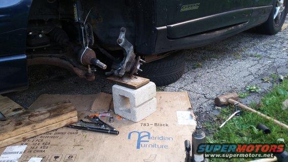 Car's front suspension assembly supported by cinder blocks and wood, with tools nearby