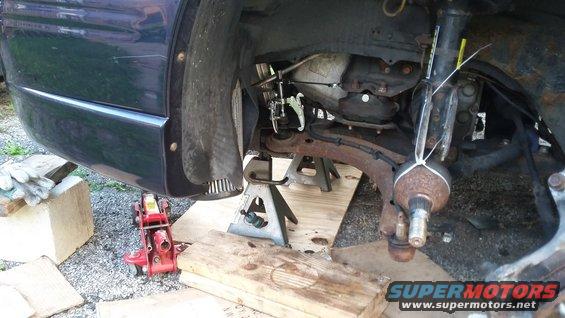 Front corner of a vehicle raised on a floor jack and stands showing rusty front suspension