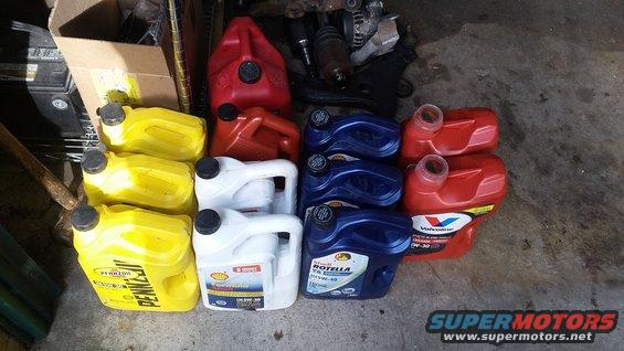 Stack of yellow, white, and blue oil containers with red gas cans