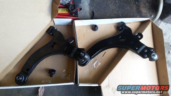 Two black control arms with ball joints and mounting hardware in cardboard boxes