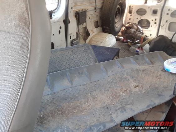 Interior of a van showing a spare tire, transmission, and diamond plate flooring