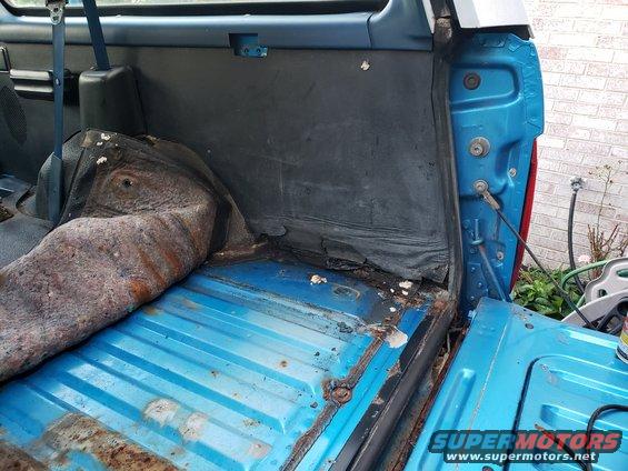 Interior cargo area of a blue SUV with worn carpeting and rusted floor