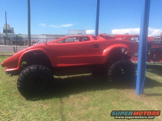 Red off-road vehicle with large tires and a modified body, seen from the side