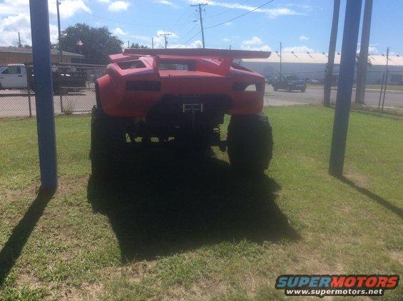 Red custom monster truck with large spoiler and oversized tires, rear view