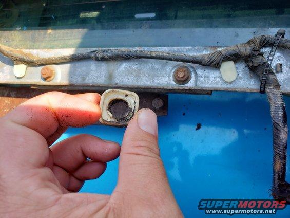 Hand holding a white plastic window regulator clip with a dark center, near metal bracket and wiring