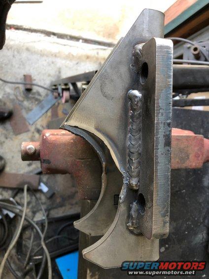 Welded metal bracket held in a vise, showing rough welds and two mounting holes