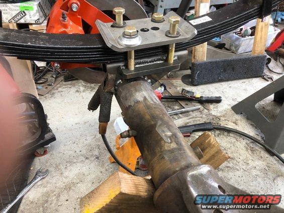 Close-up of a leaf spring attached to a metal axle assembly with bolts and welding