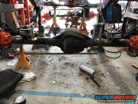 vehicle's rear axle assembly on jack stands in a garage, with tools and parts scattered around