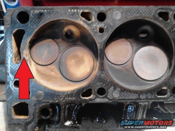 Close-up of an engine cylinder head with valves visible. A red arrow points to a damaged area