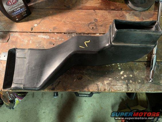 black plastic air duct with yellow markings, sitting on a wooden surface next to a bottle of transmission fluid