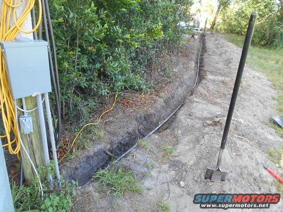 electrical box and conduit next to a dug trench with a shovel