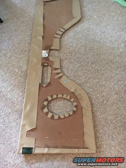 Cardboard template for a vehicle door panel, laid out on carpet. It has cutouts for a speaker and window crank