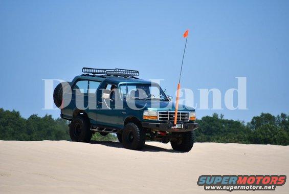Green Ford Bronco on sand dunes with an orange flag on a pole