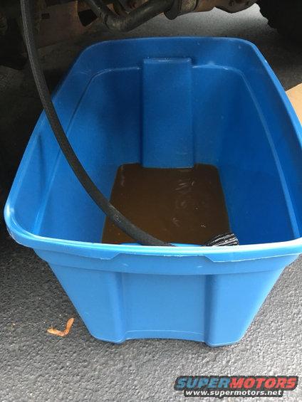 Blue drain pan collecting brown fluid from a hose under a vehicle