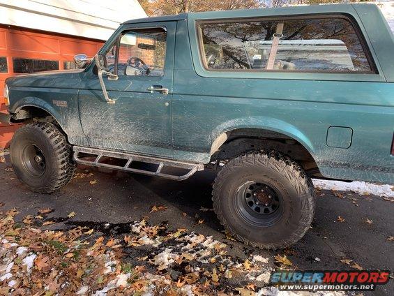 Green Ford Bronco with aftermarket side steps and large tires parked outside a garage