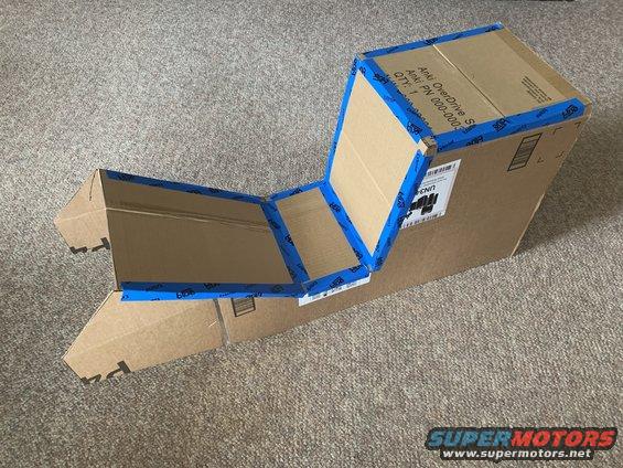 Cardboard box assembled into a seat-like structure with blue tape, on a carpeted floor