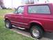 1994 Ford Bronco - A red Ford Bronco is seen from the side, parked next to a grassy area.