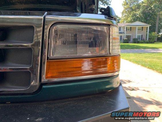 Green Ford truck front end with chrome grille and amber turn signals. Hood is up. House in background