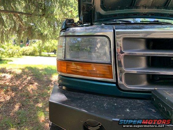 Green Ford truck front end with hood open, showing chrome grille and headlight