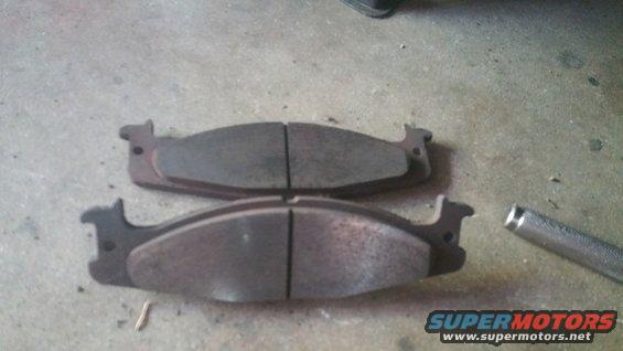 Two brake pads on concrete floor, one with a metal rod nearby