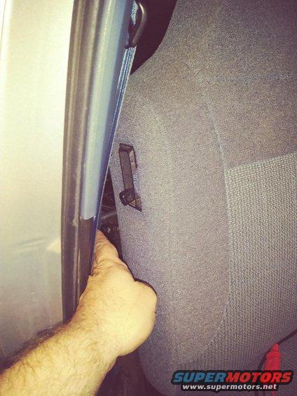 Close-up of car seat fabric and a blue door frame with a hand pointing into the gap