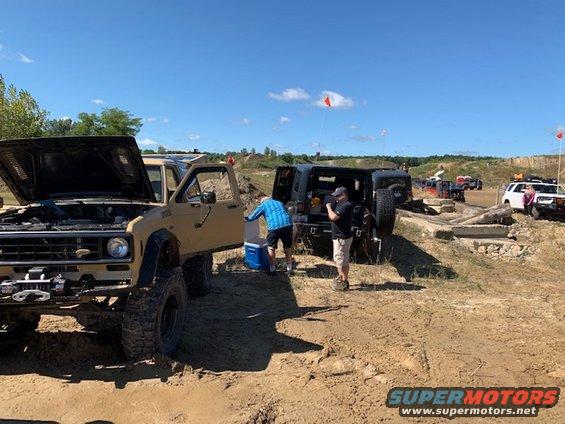 Several off-road vehicles gathered on a dirt track with people around them