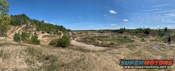 Off-road park with dirt tracks and hills under a blue sky. Some vehicles are visible in the distance