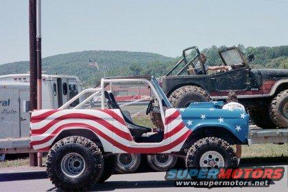 Modified Ford Bronco with American flag paint, parked next to a Jeep