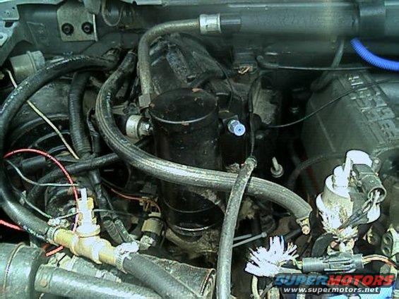 Engine bay detail showing hoses, a black cylindrical component, and electrical connections