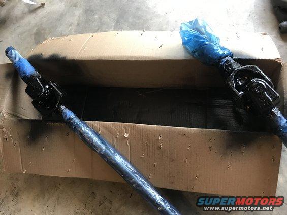 Two painted steering shafts in a cardboard box, one with blue plastic wrap on the end