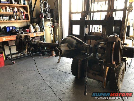 Vehicle axle assembly being lifted by a forklift in a garage