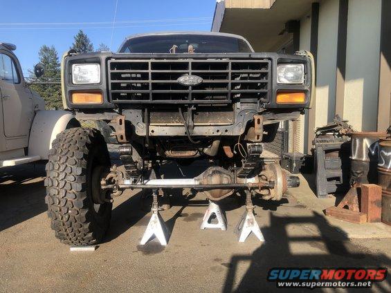 Ford truck front end, missing grille and bumper, on jack stands. Another vehicle is parked to the left