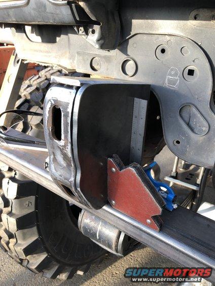 Close-up of a vehicle's frame with a metal bracket being welded, a ruler is attached to measure