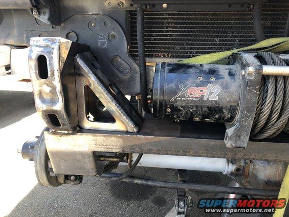 Custom steel bracket welded to vehicle frame, holding a Smittybilt XRC 12 winch with steel cable