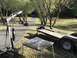 1989 Ford Bronco - An engine hoist, a flatbed trailer, and a weathered table are set up outdoors on a paved path.
