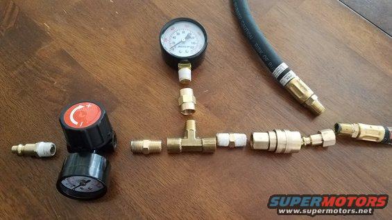 Air pressure gauge, regulator, T-fitting, and hose connectors laid out on a wooden surface