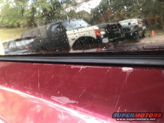Scratched red vehicle exterior, reflection of white and black trucks in window
