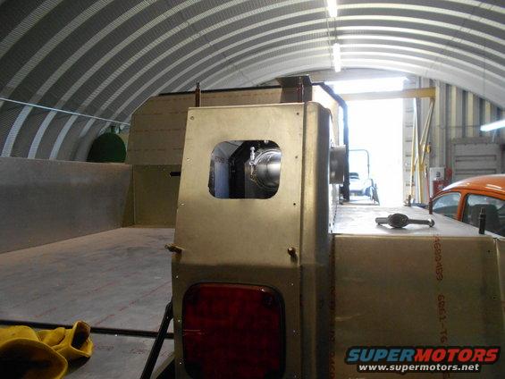 Interior of a workshop showing a custom truck bed under construction, with an orange car visible in the background