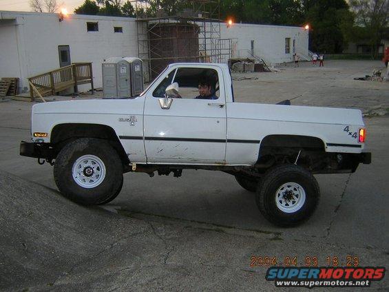 White pickup truck with lifted suspension and large tires, driver visible inside