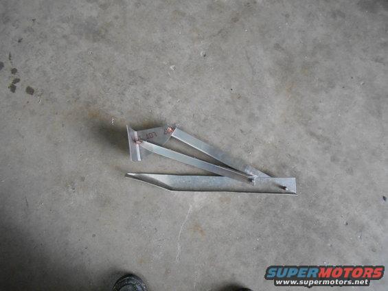 Metal bracket with some writing on it, lying on a concrete floor