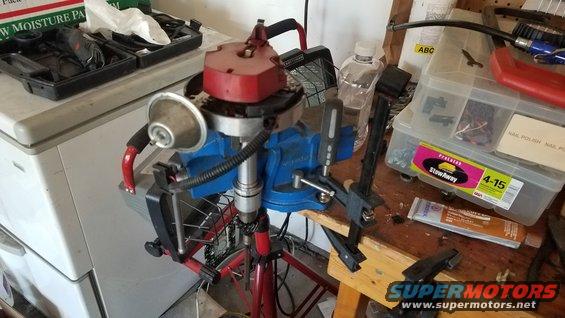 Automotive distributor held in a blue vise on a workbench with tools and parts nearby