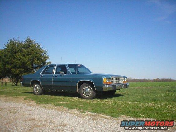 Teal 1987 Ford Crown Victoria parked on a gravel road next to a grassy field